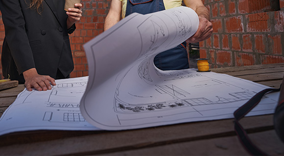 two people discussing architectural blueprints with a partially unrolled plan on a wooden table showcasing design details and construction elements for a project evaluation
