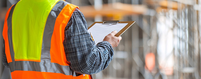 construction worker wearing a safety vest holding a clipboard with a checklist monitoring seven aspects of the project