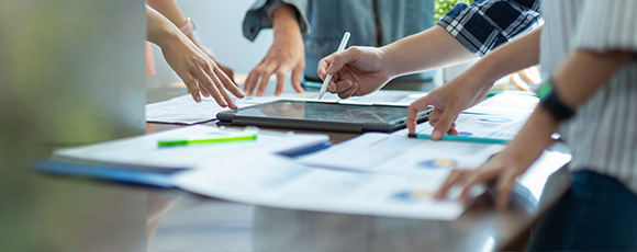 multiple hands collaborating on documents and a tablet in a business setting focused on teamwork three strategies and planning