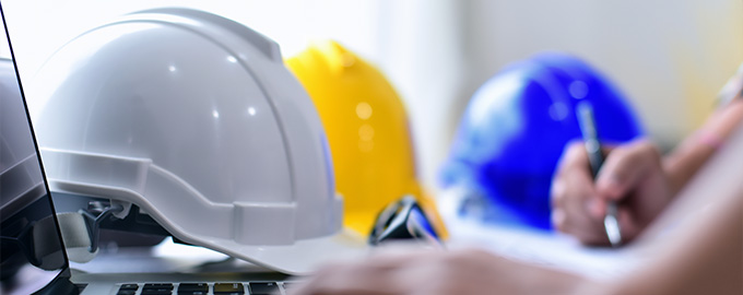 white construction helmet on a laptop with yellow and blue helmets in the background someone writing showing work safety and collaboration in construction projects 3 types of helmets